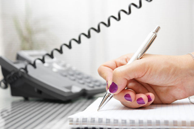 Image showing lady's hand with pen writing on pad whilst using the phone. Block is about people requiring translation and interpretation services.